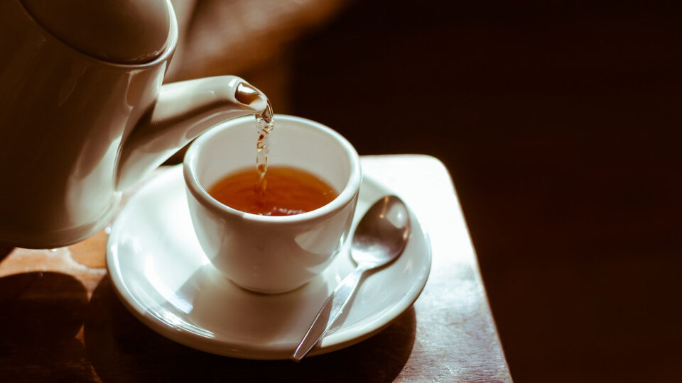 image od tea being poured from a tea pot, into a cup with saucer